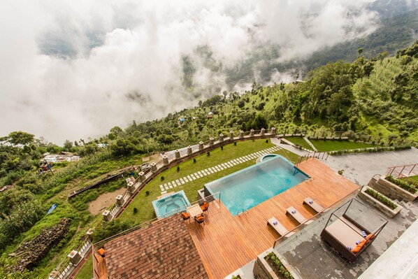 A pool area with a wooden deck, lounge chairs, and a hot tub.