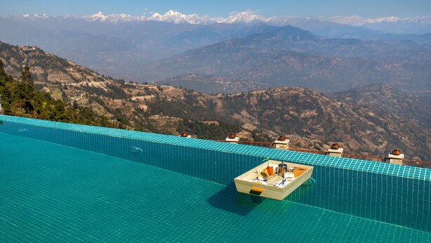 Una piscina infinita con una caja de madera que contiene bebidas y aperitivos, con vistas a un paisaje montañoso.