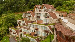 Un hotel moderno de varios pisos con balcones, jardines escalonados y un exuberante fondo verde.
