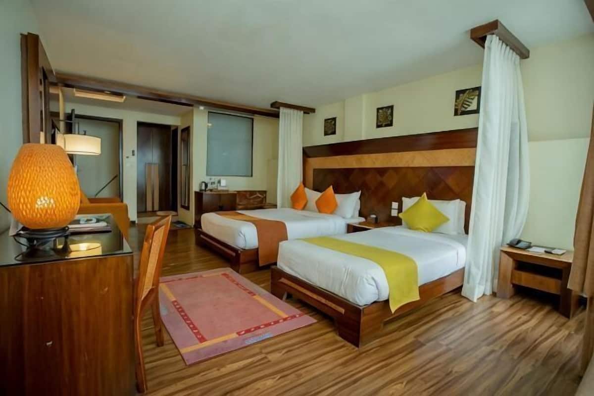 A hotel room with two beds, a desk, a lamp, and a chair.