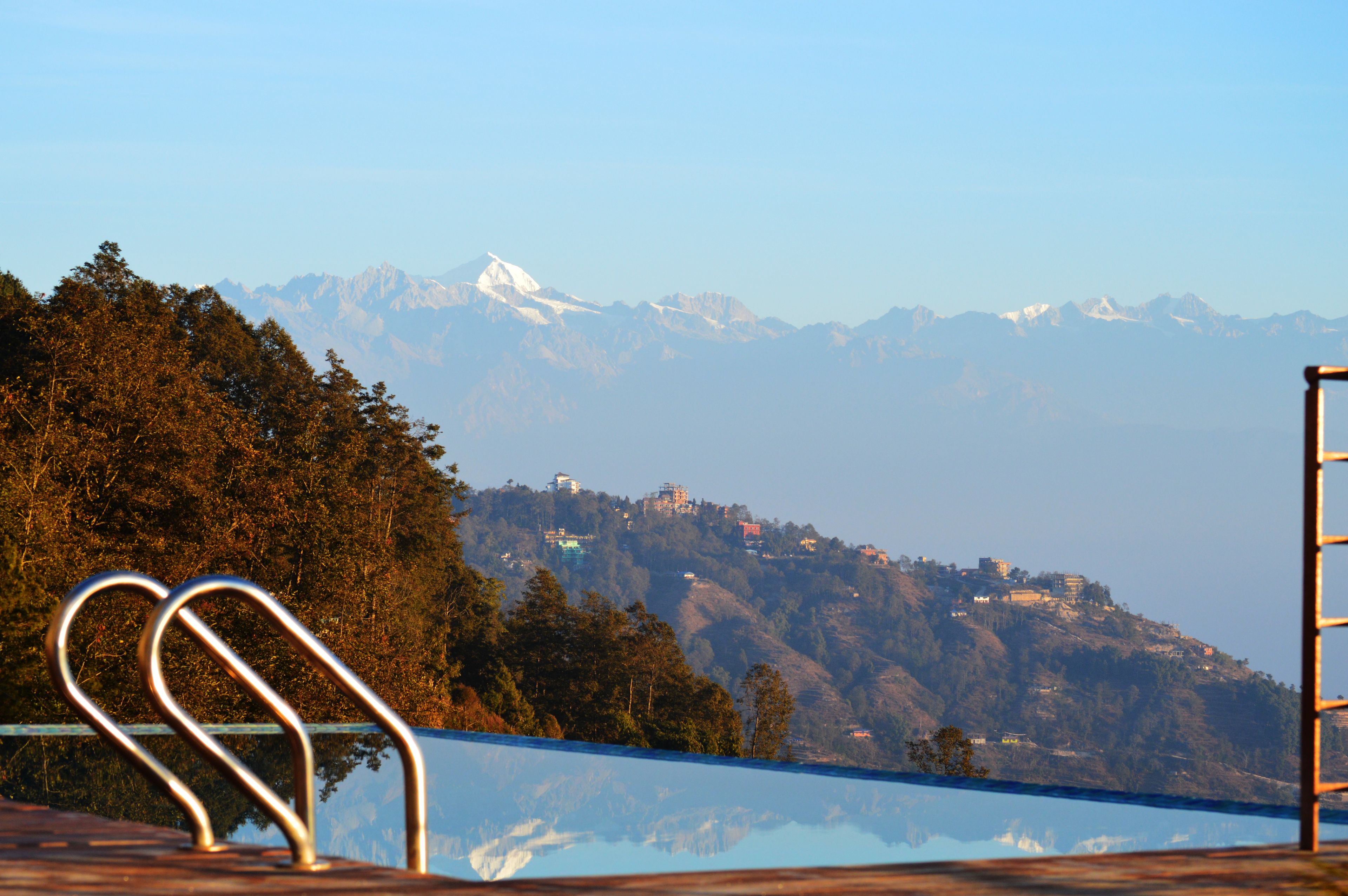 A pool with metal railings, surrounded by trees and a mountain range in the background.