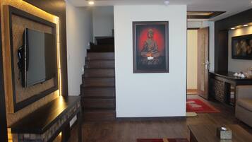 A modern living room with a staircase, a framed Buddha statue, and a flat-screen TV mounted on a textured wall.