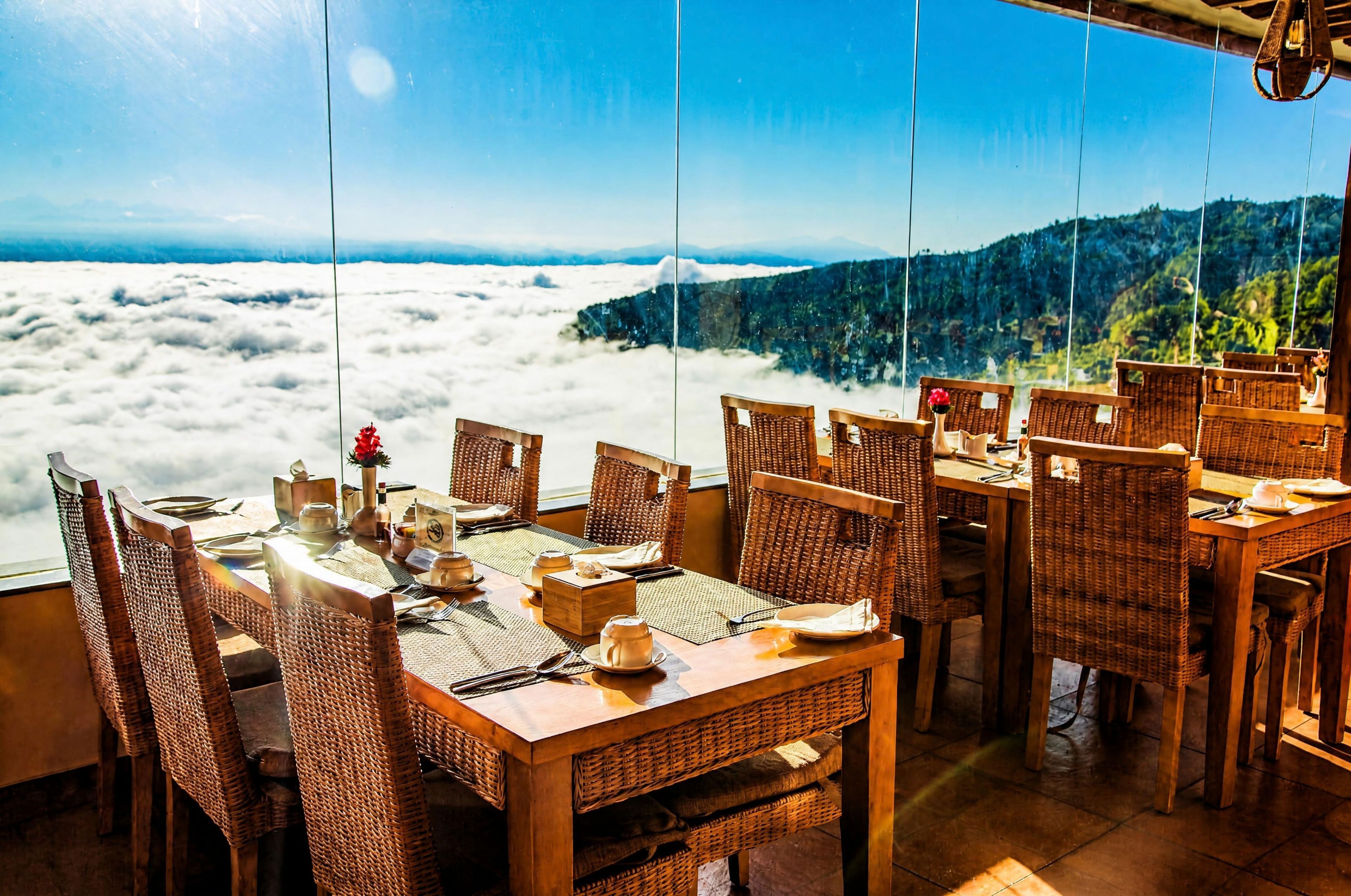 A dining area with wicker furniture and a table set for a meal, overlooking a mountainous landscape.