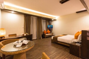 Una habitación de hotel con una cama, una mesa de comedor con sillas, un televisor y un ventanal con cortinas.