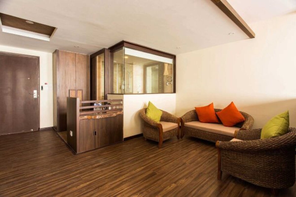 Un salon moderne avec un plancher en bois, un meuble encastré en bois, un grand miroir et deux canapés en osier avec des coussins.