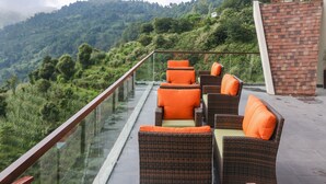 Un balcón con muebles de mimbre y cojines naranja, con vistas a una exuberante ladera verde.