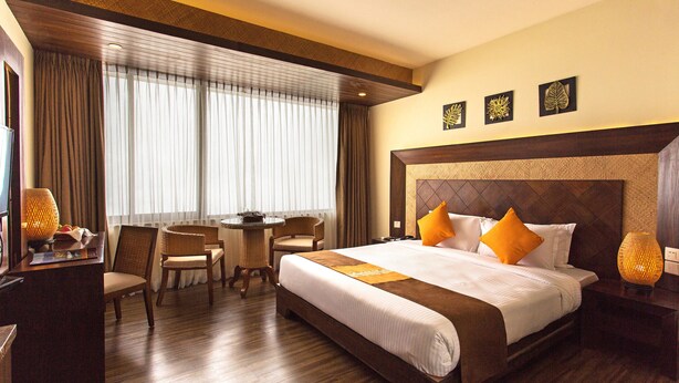 Habitación de hotel con una cama grande, un escritorio con lámpara, una silla y una ventana con cortinas.