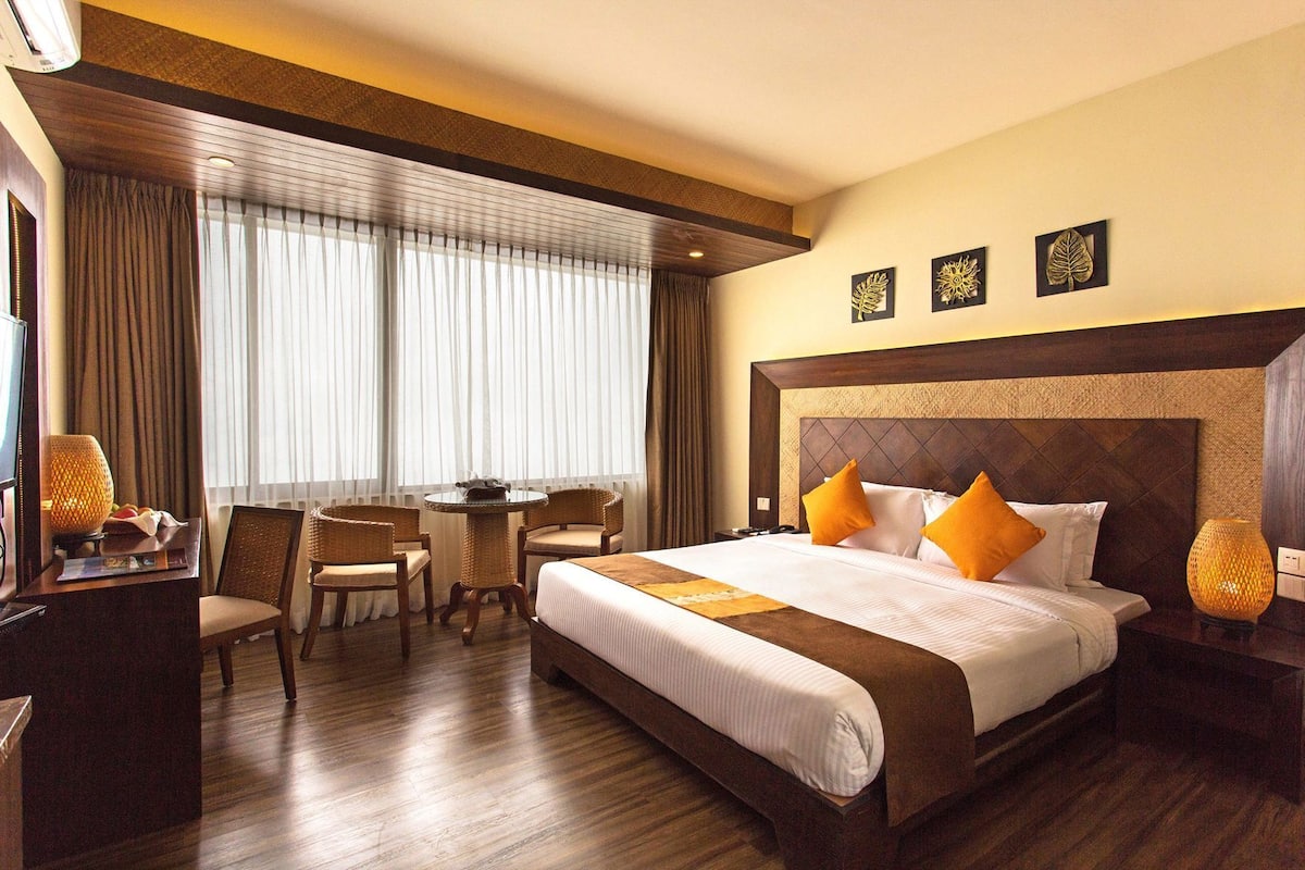 A hotel room with a large bed, a desk with a lamp, a chair, and a view of the outdoors.