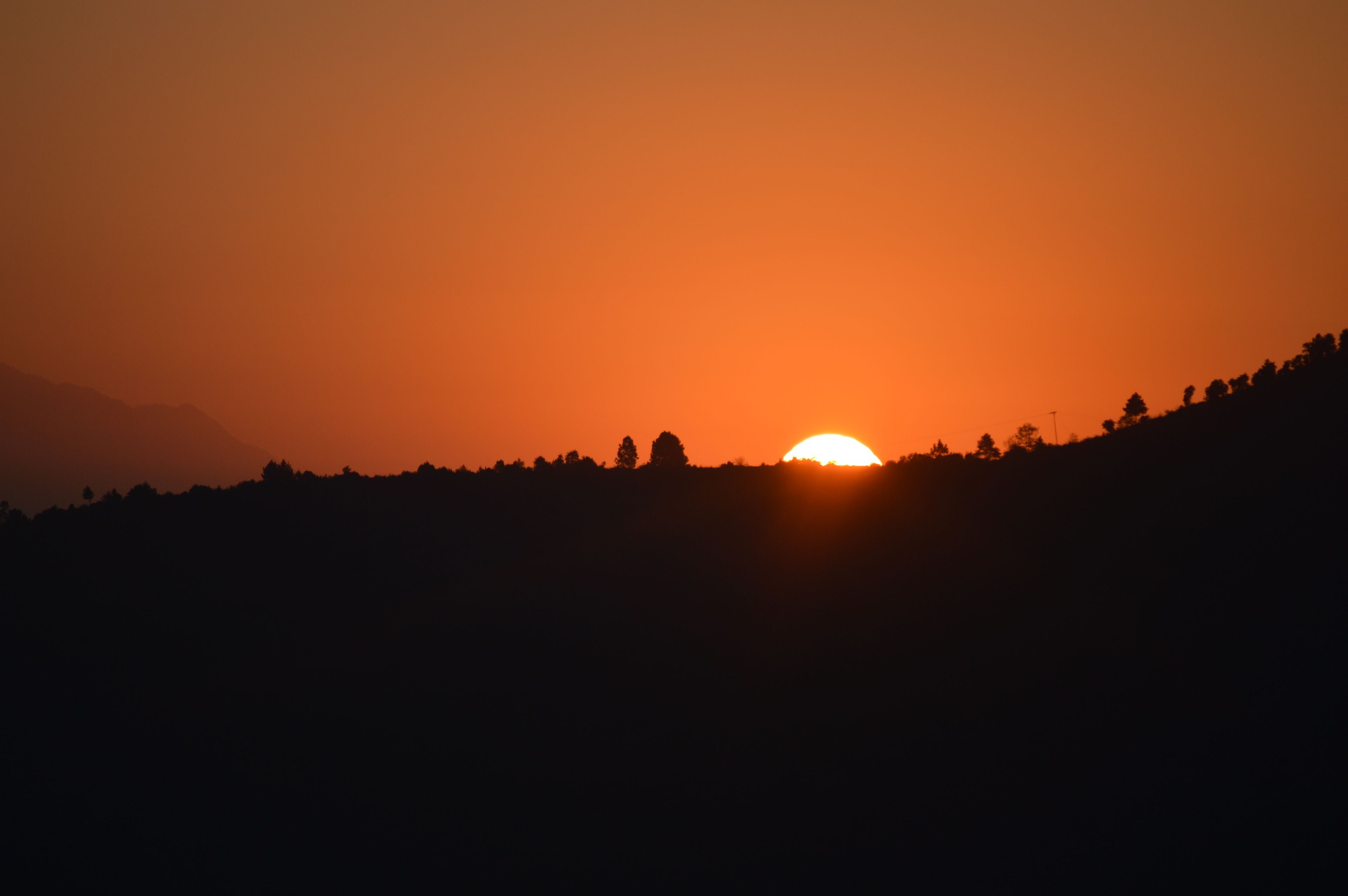 Auringonlasku kumpuilevan maiseman yllä.