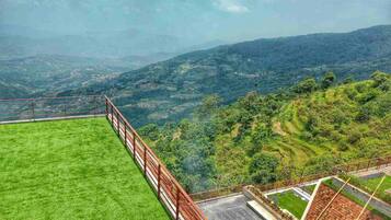 Una terraza con césped y barandilla de metal que domina un paisaje montañoso.