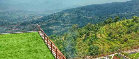 A grassy terrace with a metal railing overlooking a hilly landscape.