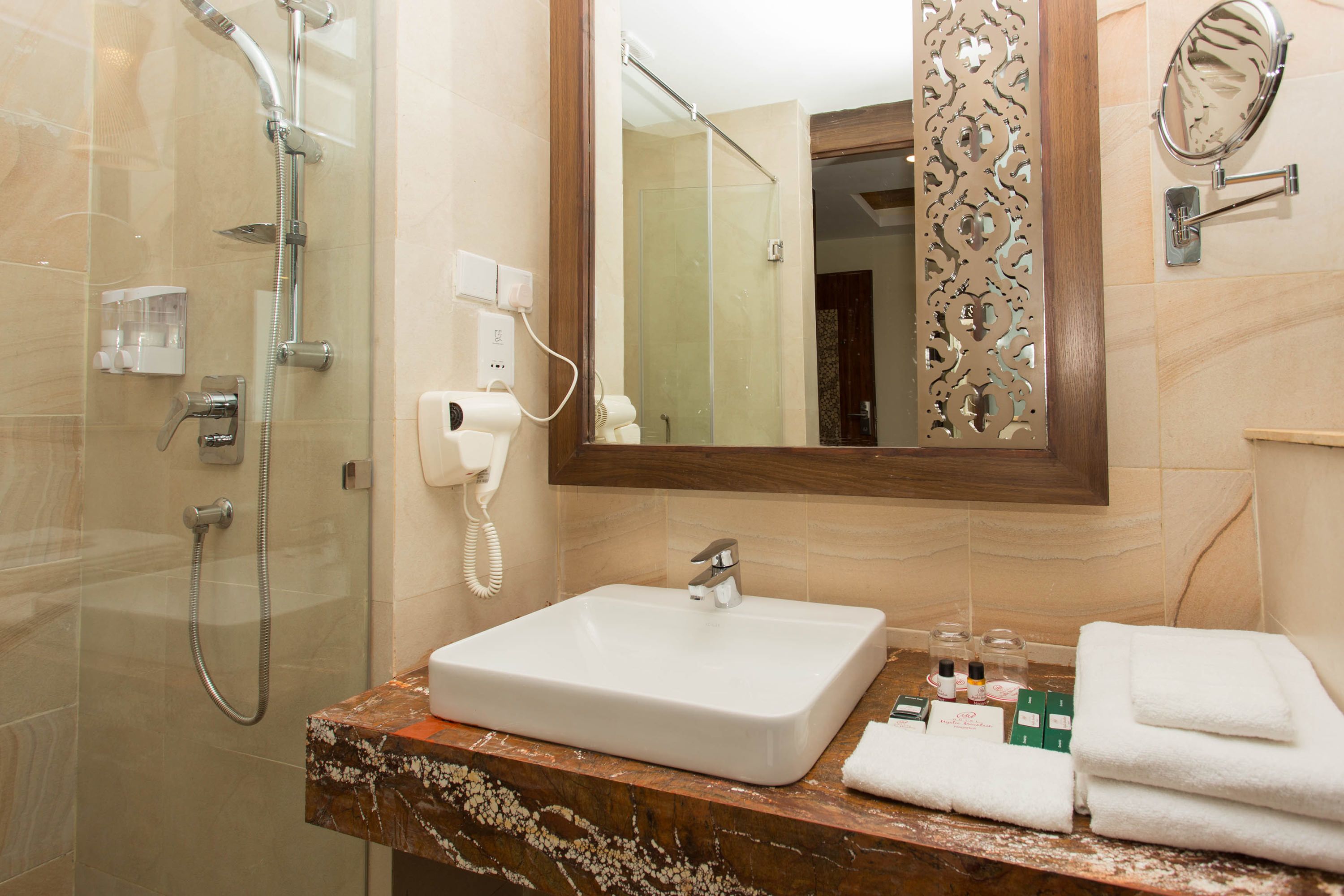A bathroom with a glass-enclosed shower, a white sink, and a mirror with a decorative frame.