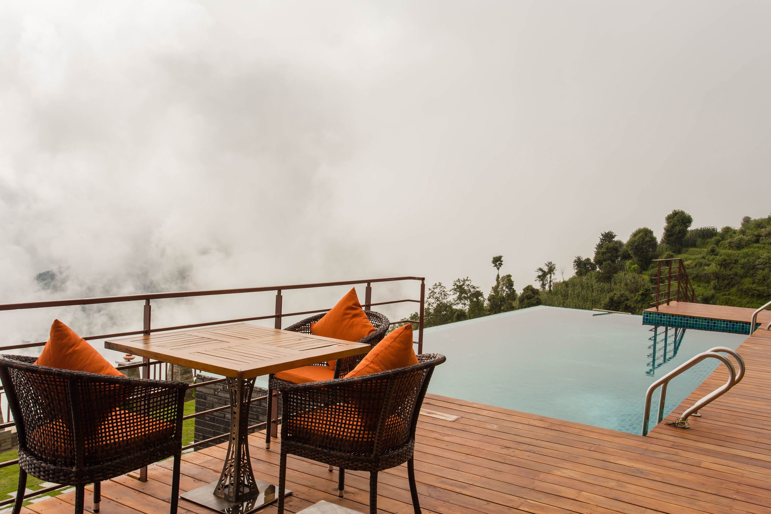 A wooden deck with wicker chairs and a table, overlooking a pool.