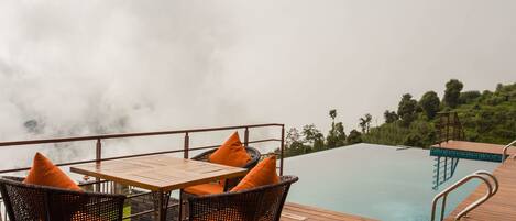 A wooden deck with wicker chairs and a table, overlooking a pool.
