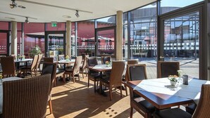 Un comedor interior con mesas y sillas, ventanas amplias y vistas al exterior.