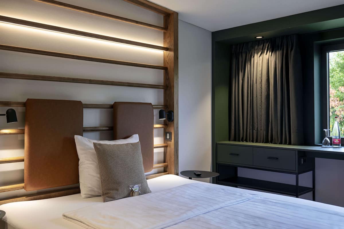 A hotel room with a bed, a nightstand, a desk, and a window with curtains.