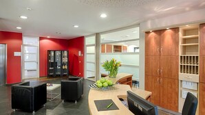 Una zona de recepción moderna con un mostrador curvo, sillas de cuero negro, una mesa de madera con manzanas verdes y un florero.