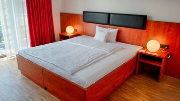 Habitación de hotel moderna con una cama grande, cabecera de madera, mesitas de noche con lámparas y vistas a través de un ventanal amplio.