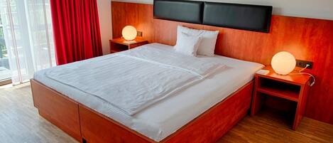 Quarto de hotel moderno com cama grande, cabeceira de madeira, mesas de cabeceira com abajures e vista pela janela.