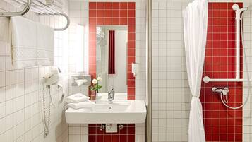 Un baño con lavamanos blanco, paredes con azulejos rojos, ducha con cortina blanca y un toallero con toallas dobladas.