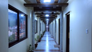 A long, narrow hallway with a view of buildings and mountains through large windows on one side. - Hotel Queens Park (Pokhara)