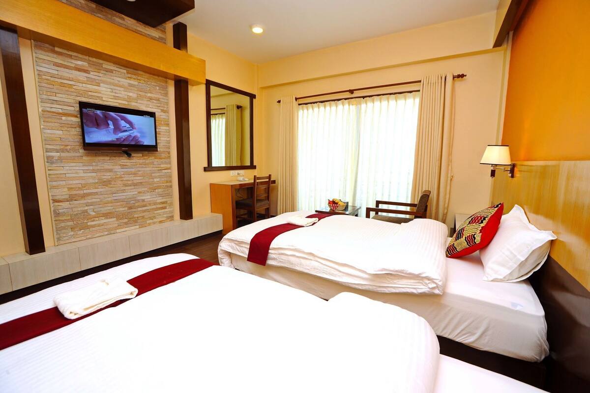A hotel room with two beds, a TV on the wall, a desk, and a chair.
