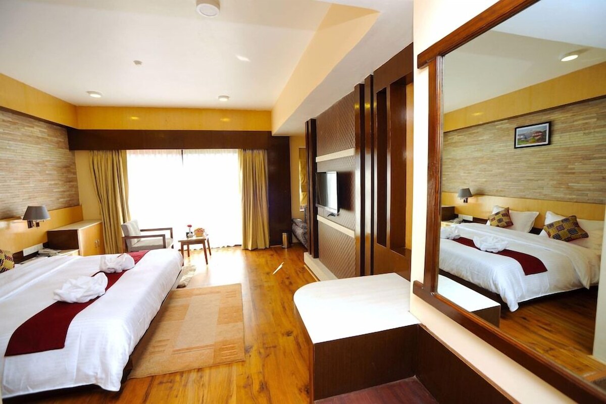 A hotel room with two beds, a TV, a desk, and a large mirror.