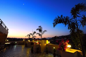A rooftop terrace with potted plants, outdoor seating, and a view of the city skyline at dusk. - Hotel Queens Park (Pokhara)