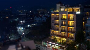 A multi-story hotel with balconies, a ground-level restaurant, and a view of the surrounding urban area. - Hotel Queens Park (Pokhara)