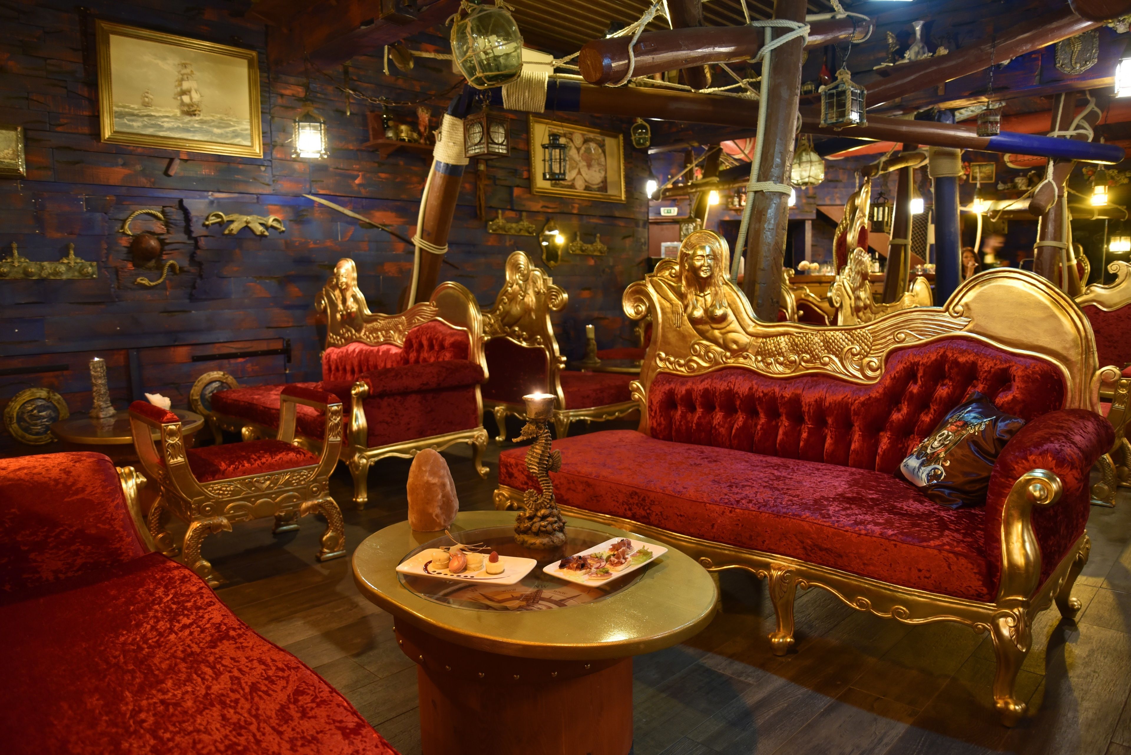 Ein luxuriöser Raum mit kunstvollen Möbeln, darunter ein rotes Samtsofa und goldene Stühle, sowie ein Tisch mit angerichteten Speisen.