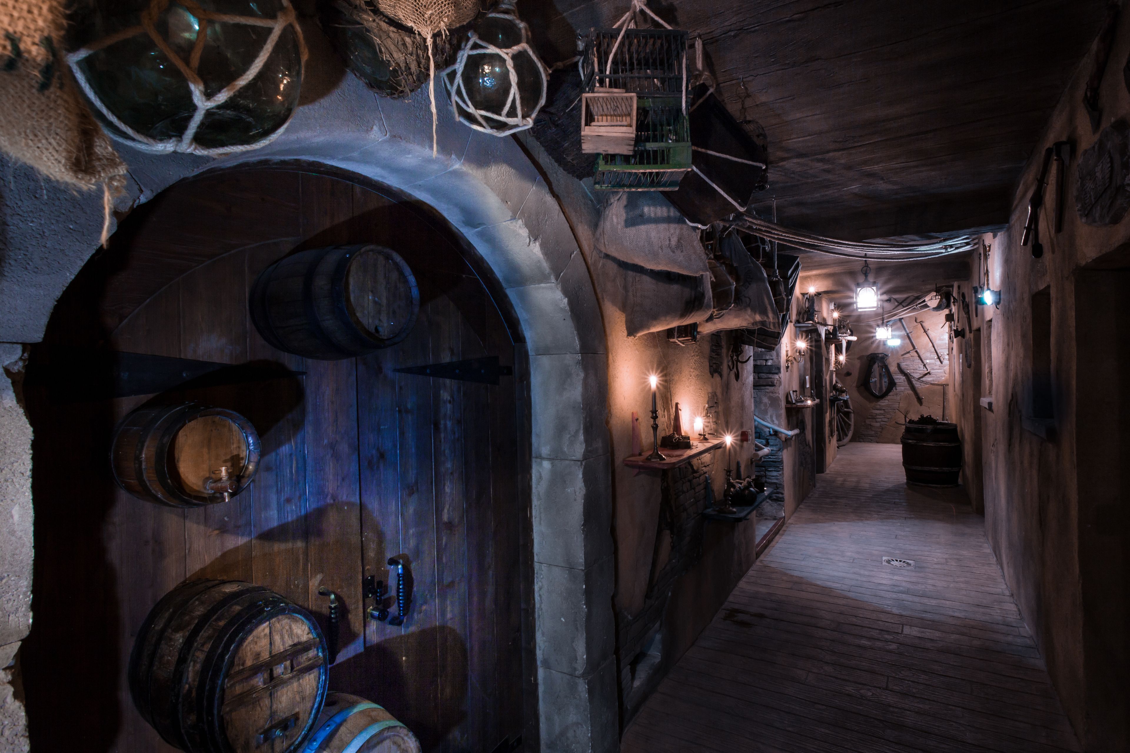 A narrow, dimly lit corridor with wooden barrels and a rustic, stone wall.