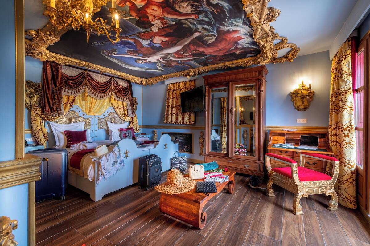 Una habitación lujosa con cama, escritorio, silla y un mural en el techo.
