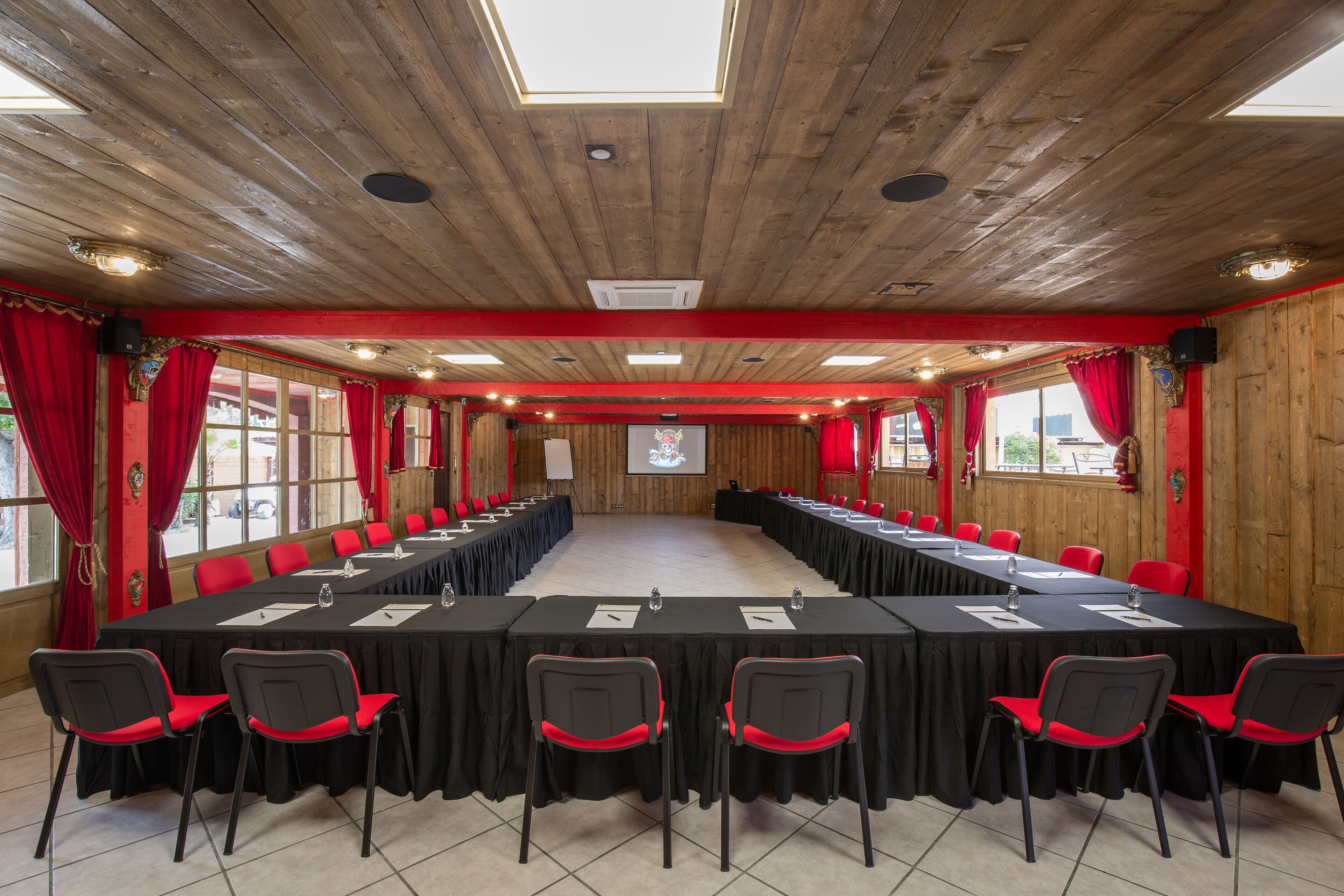 Une salle de conférence avec une longue table, des chaises rouges et des murs en bois.