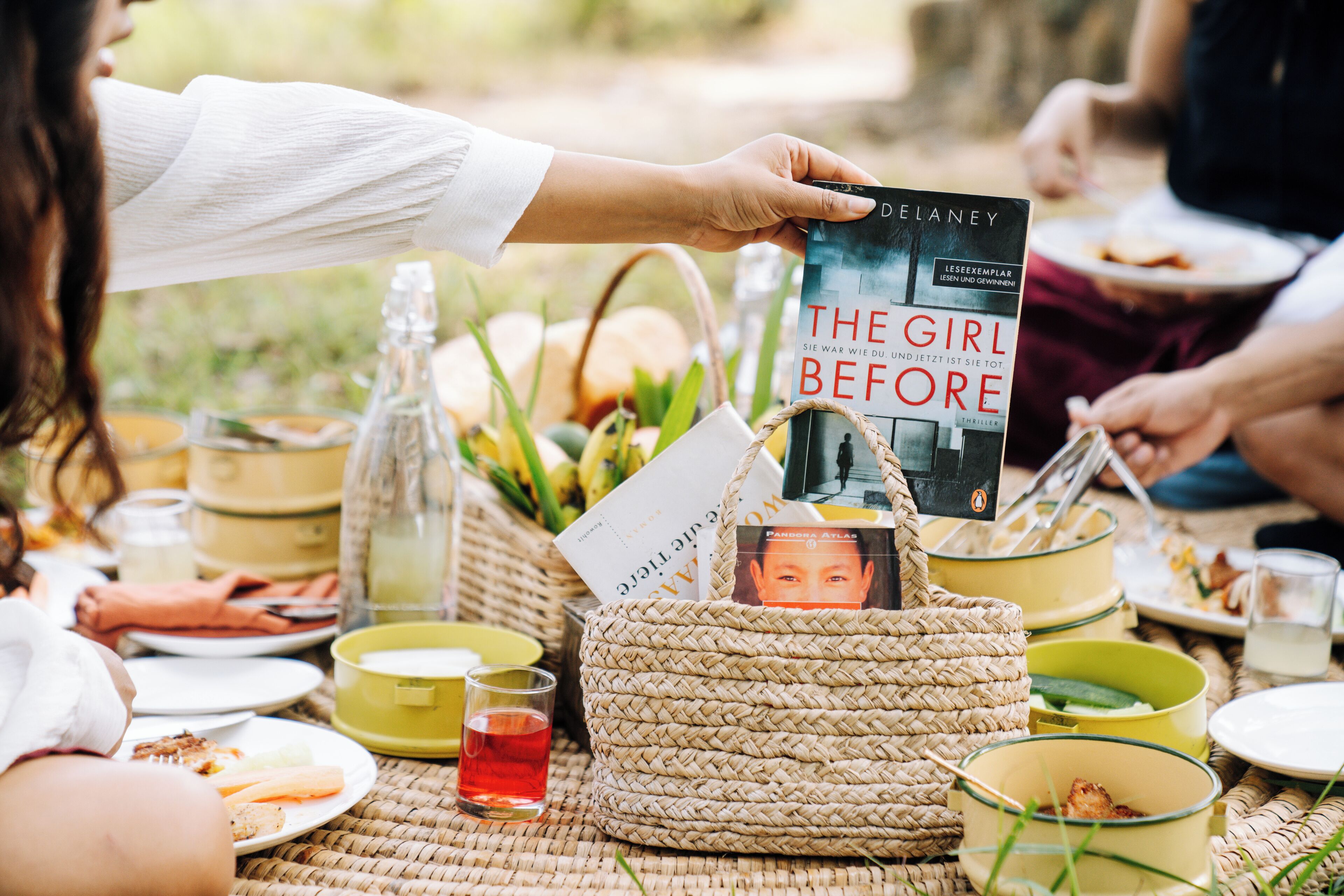 Un'area picnic con un cesto di vimini, libri e cibo su un tavolo.