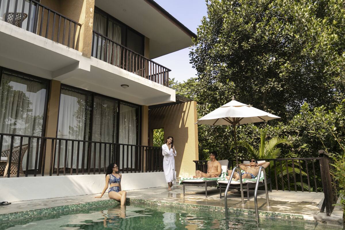 A pool area with a lounge chair, a sun umbrella, and a building with balconies.