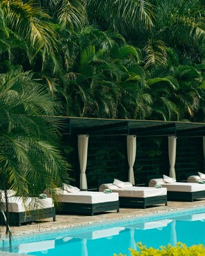 A poolside area with two lounge chairs and a canopy, surrounded by lush palm trees. - Kasara Resort - Chitwan National Park (Bharatpur)