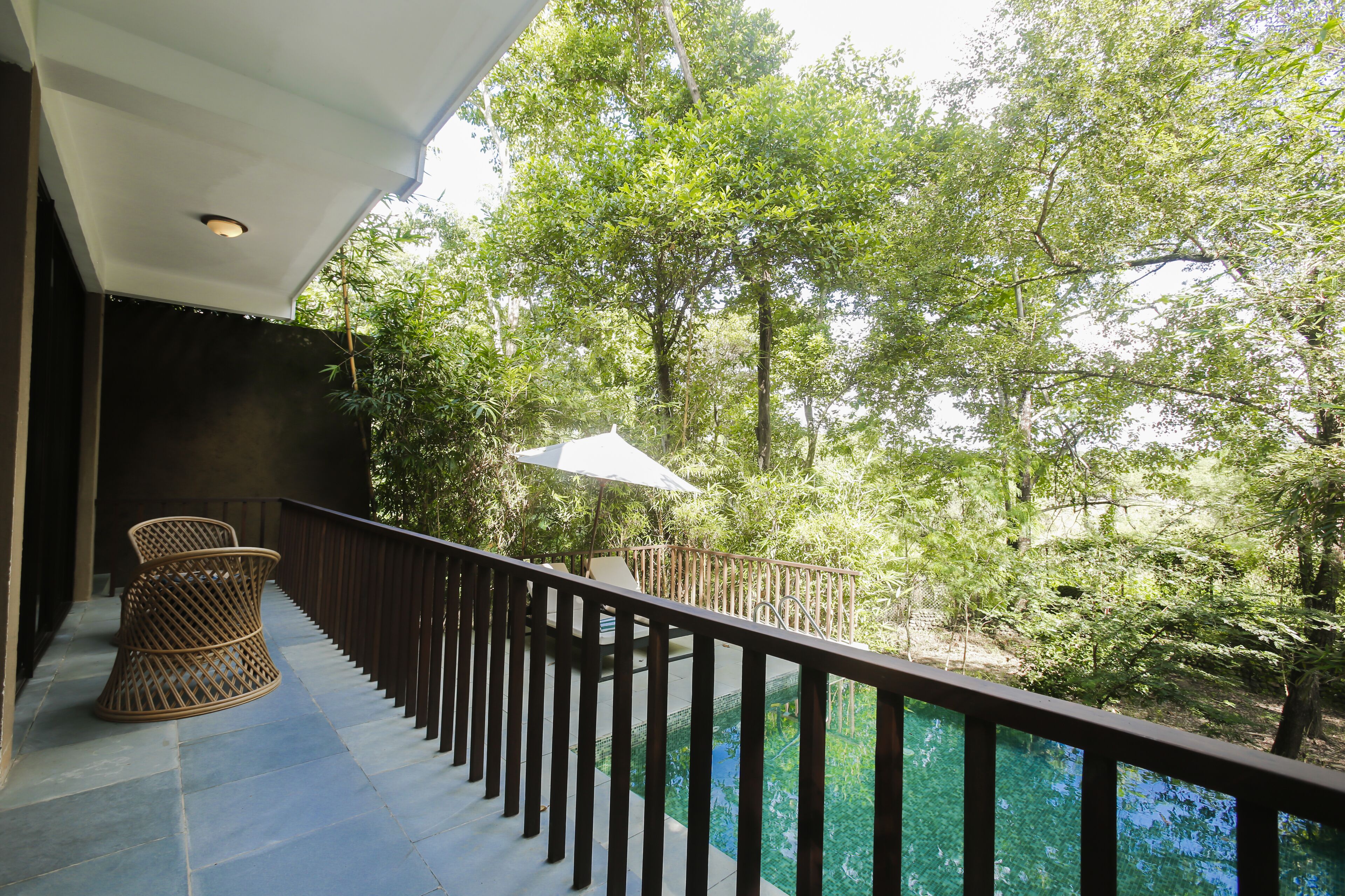 A balcony with a view of a forested area and a pool.