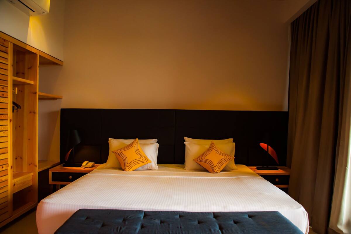 A hotel room with a large bed, two bedside tables, a wooden wardrobe, and a dark headboard.