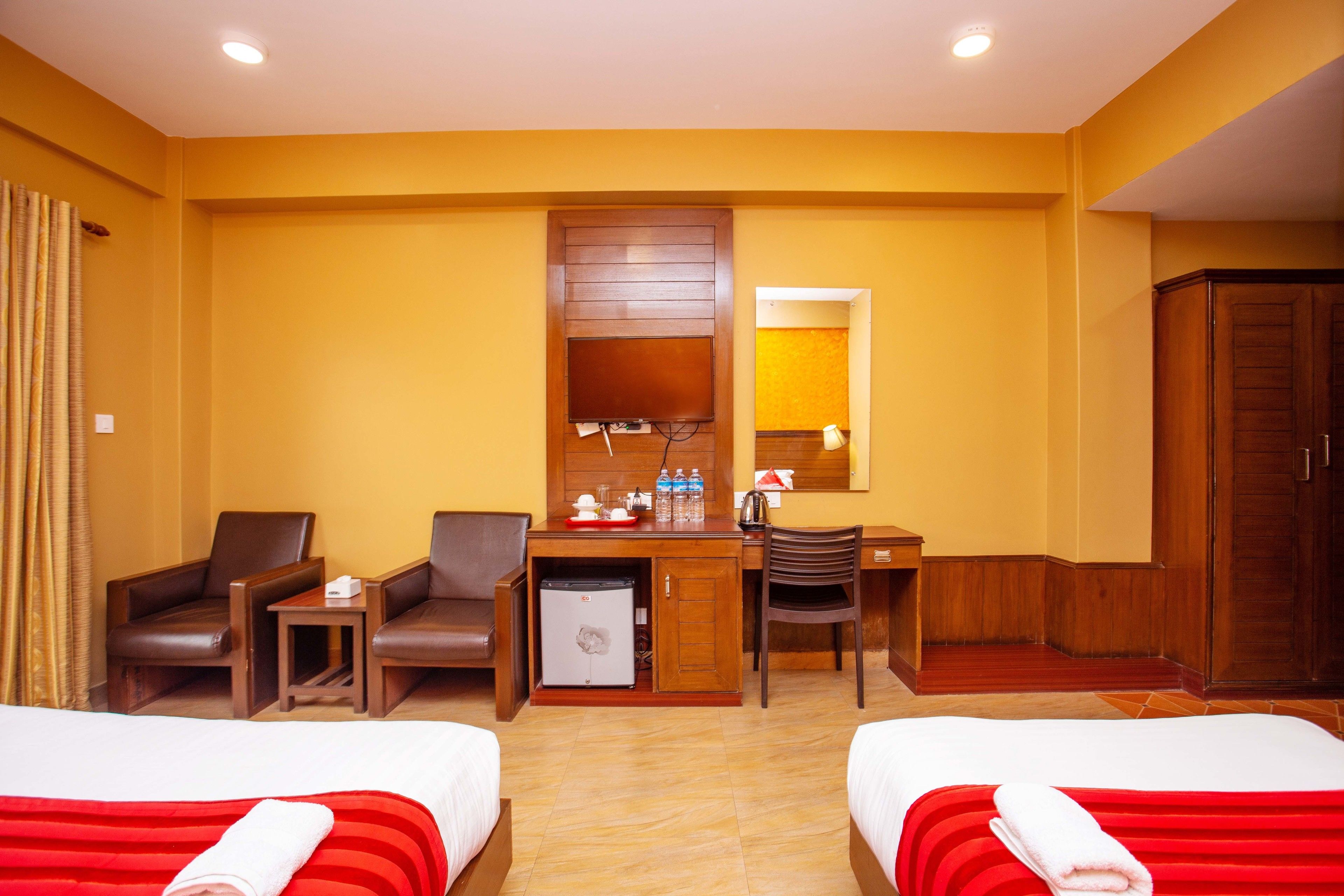 A hotel room with two beds, a desk, a refrigerator, and a wardrobe.