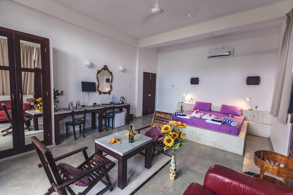 Une chambre d’hôtel moderne avec un coin repas, un lit avec une literie violette et un grand miroir.
