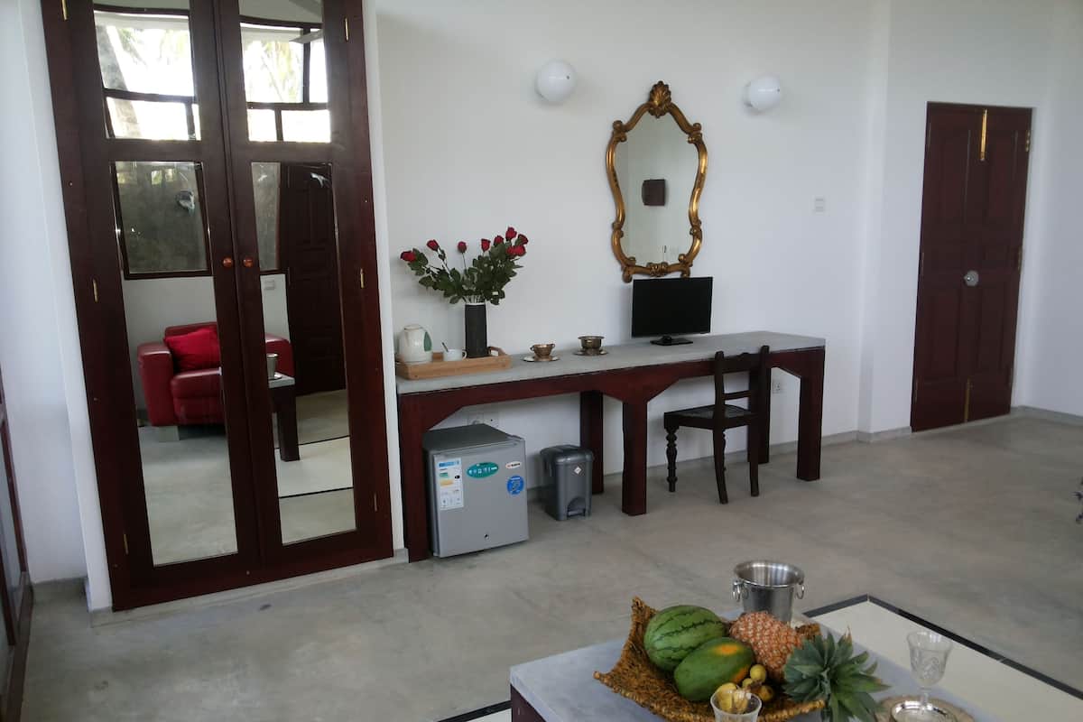 Une pièce comprenant un bureau, une chaise et un petit réfrigérateur. Il y a un miroir au mur et une porte avec un panneau en verre.
