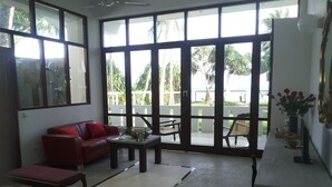 Un amplio salón con un sofá rojo, una mesa de centro y vistas a un jardín a través de grandes ventanales.
