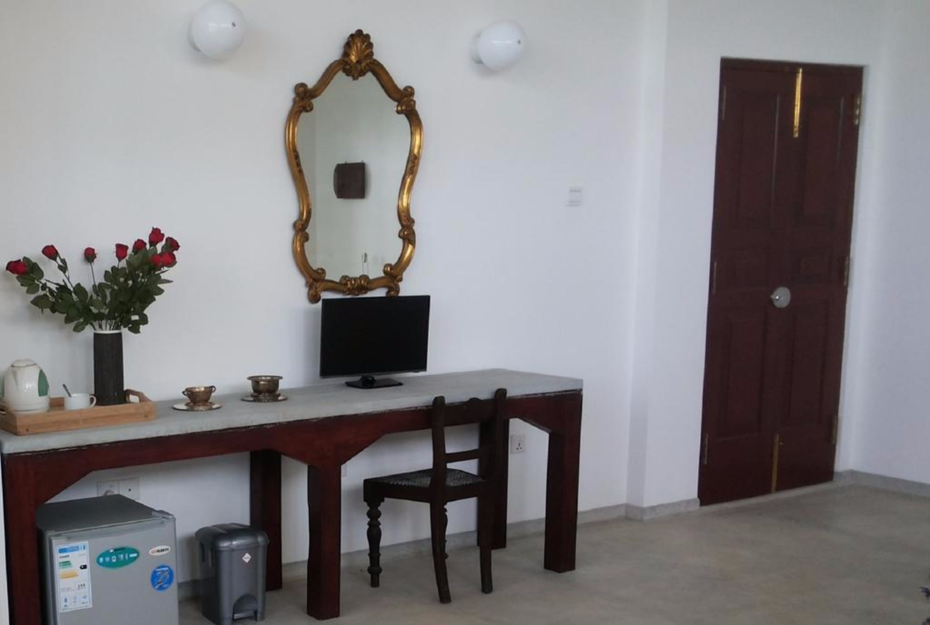 A room with a desk, chair, television, and a large mirror on the wall.