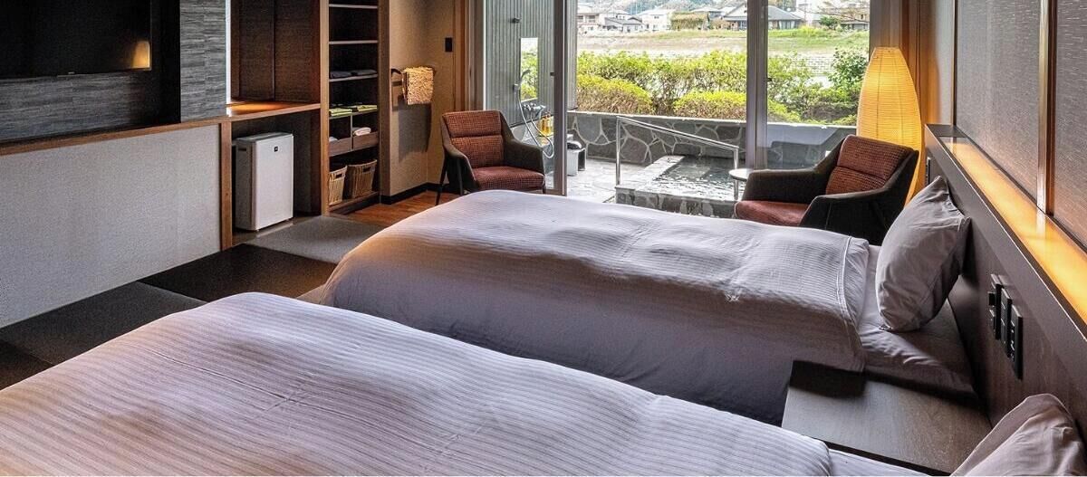 Ein modernes Hotelzimmer mit zwei Betten, einem kleinen Schreibtisch, einem Stuhl und einem Balkon mit Aussicht.