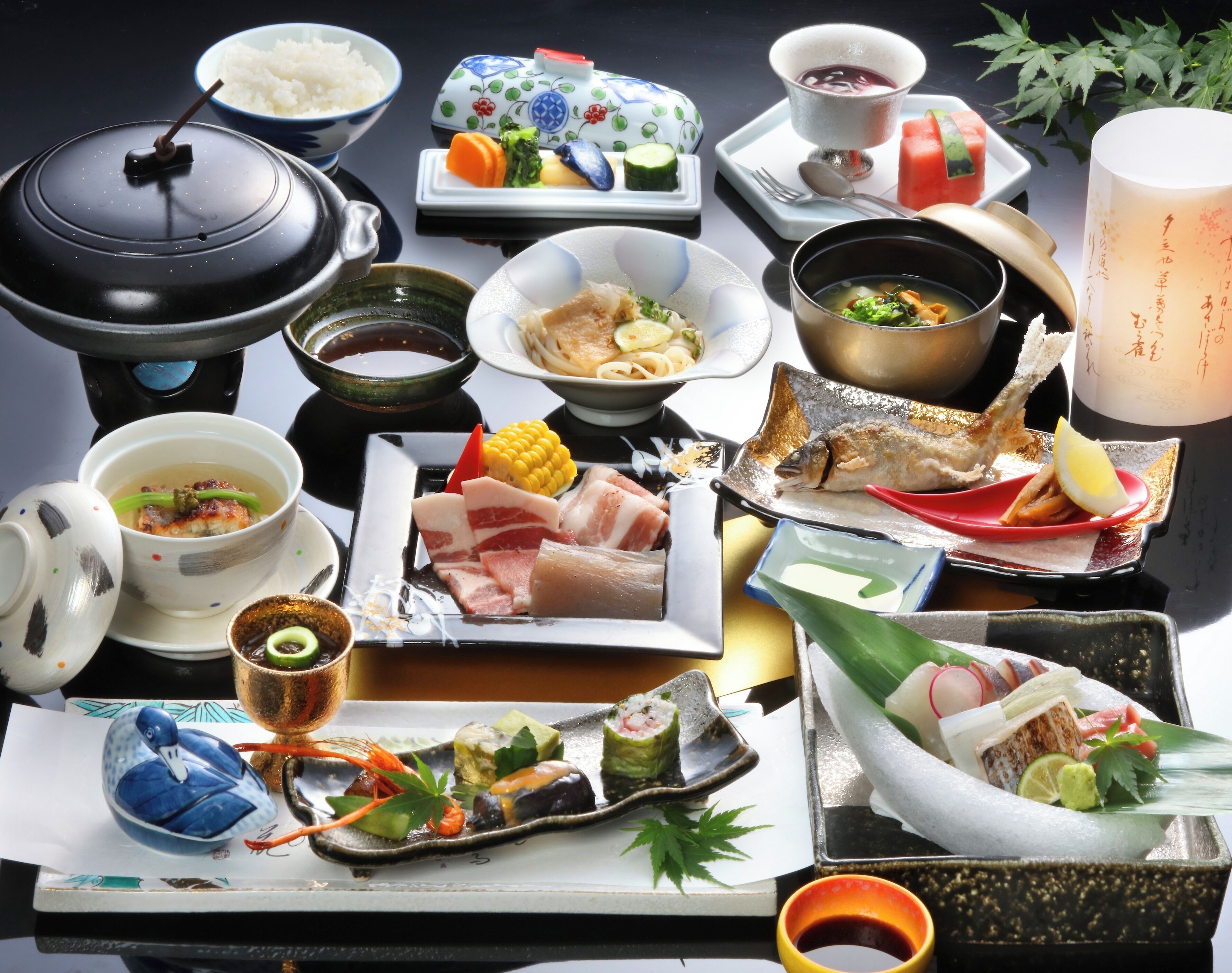 Diverse Japanse gerechten en bestek op een tafel, waaronder sushi, sashimi en een hete pot.