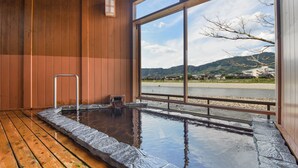 Ein Thermalbadbereich mit Holzwänden und einem großen Fenster mit Blick auf einen Fluss und Hügel.