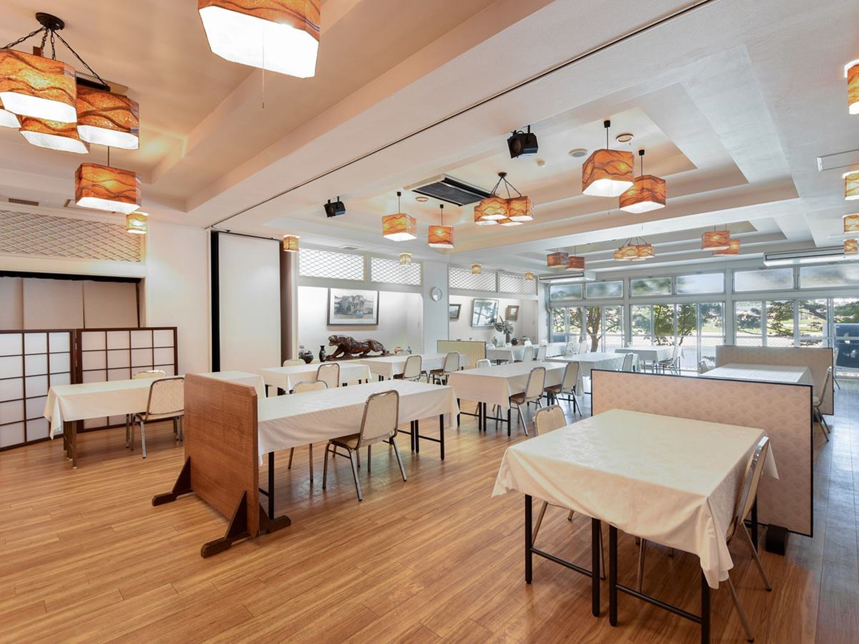 A spacious dining area with multiple tables and chairs, large windows, and modern pendant lighting.