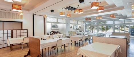 A spacious dining area with multiple tables and chairs, large windows, and modern pendant lighting.