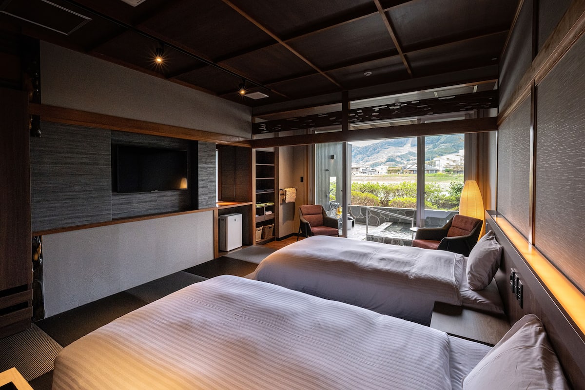 Une chambre d’hôtel moderne avec deux lits, une télévision, un bureau et une vue sur un paysage montagneux.