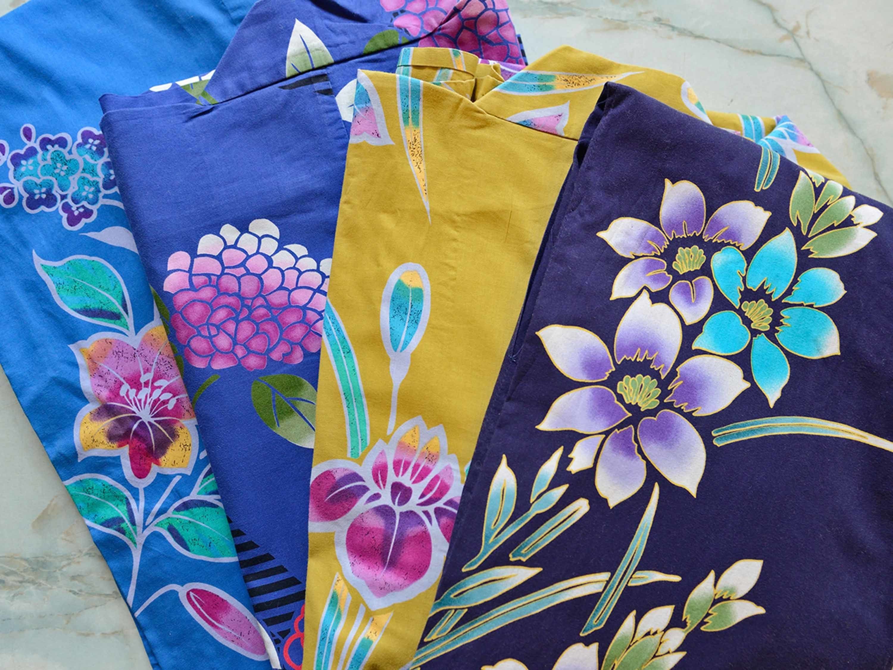 Three folded fabrics with floral patterns in blue, yellow, and purple.